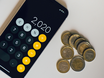 Mobiltelefon med kalkylator-app bredvid några mynt på en vit bordsskiva